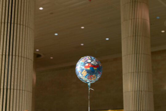 Blue welcome balloon floating indoors at airport arrivals among tall pillars. Israel
