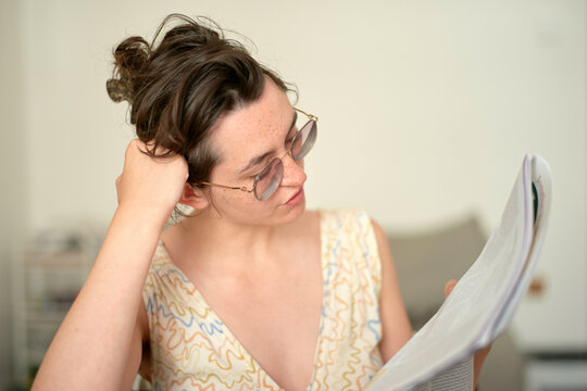 Young cute woman with sunglasses reading a newspaper, wearing a patterned sleeveless vintage dress.