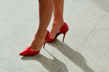 Red high heels on a tiled floor, casting a shadow in natural light.