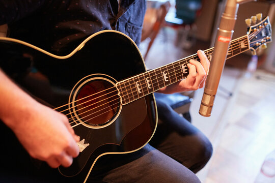 Musician strumming an acoustic guitar in a recording studio setting.