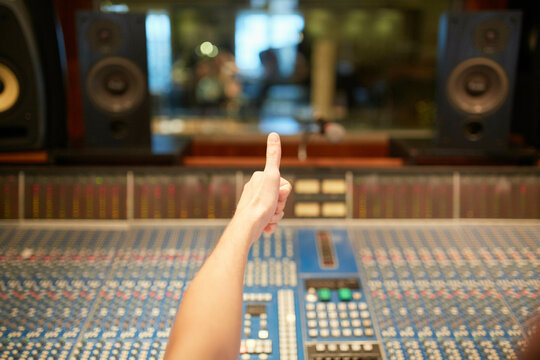 Hand giving thumbs up behind a large studio sound mixing console with speakers.