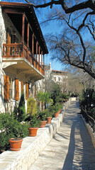 Fototapeta premium Scenic Walkway Lined With Potted Plants Leading to Charming Stone Buildings in Bright Daylight