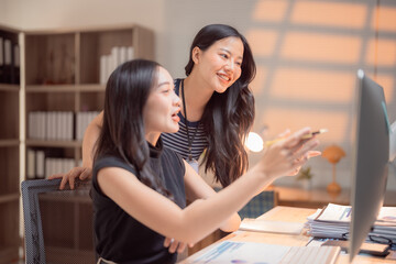 Two asian businesswomen discussing and analyzing financial data on a computer screen, working together on a project in a modern office, collaborating and sharing ideas