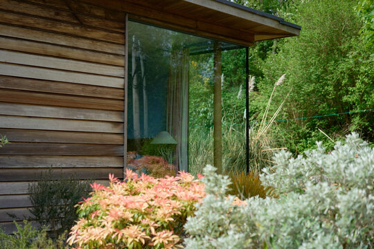 Modern wooden house with large glass window surrounded by lush garden plants and greenery. Ireland