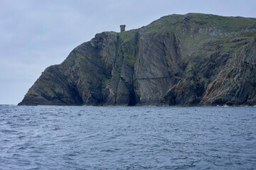 Rugged coastal cliff with a lone tower perched atop, overlooking the vast ocean below. Ireland
