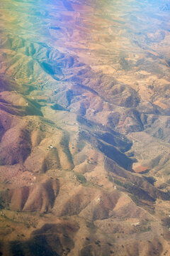 Aerial view from a plane of arid desert landscape with multicolored lighting effect on the window. Lanzarote, Spain