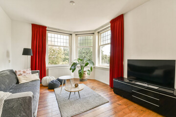 A well-lit living room featuring a comfortable gray sofa, stylish curtains, a coffee table, and a television. Natural light enhances the inviting atmosphere.