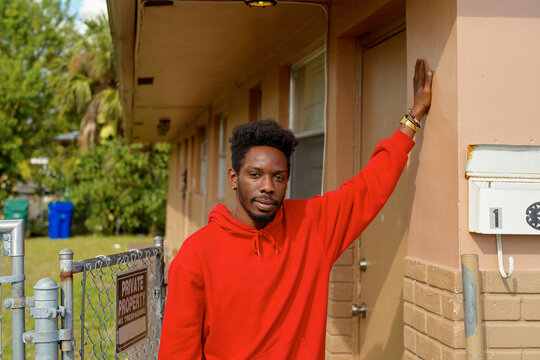 Man in red hoodie leans against a building in a suburbian area near a private property sign. Miami, Florida