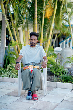 Man sitting on a chair outside, surrounded by palm trees and preparing a peanut butter sandwich. Miami, Florida
