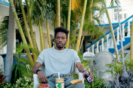 Man sitting outdoors with tree background, with a jar of peanut butter and a sandwich. Miami, Florida