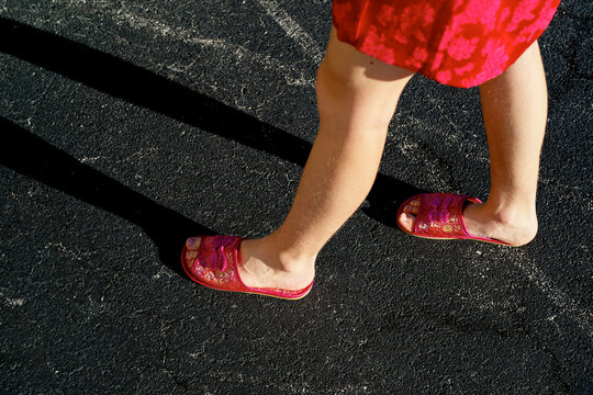Woman wearing red sandals and skirt walking on a sunlit asphalt surface. Miami, FL, USA
