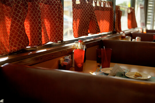 Sunlit diner booth with red-patterned curtains and empty plates on the table. Miami, FL, USA