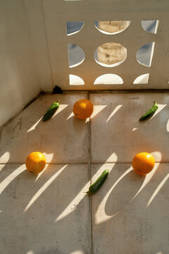 Oranges and cucumbers arranged in sunlight on a tiled floor next to a patterned wall. Miami, FL, USA