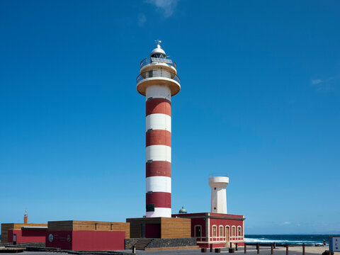Red and white striped lighthouse with outbuildings against a clear blue sky. Fuerteventura, Spain