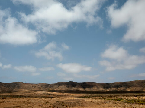 Desert landscape with rolling hills under a cloudy blue sky. Fuerteventura, Spain