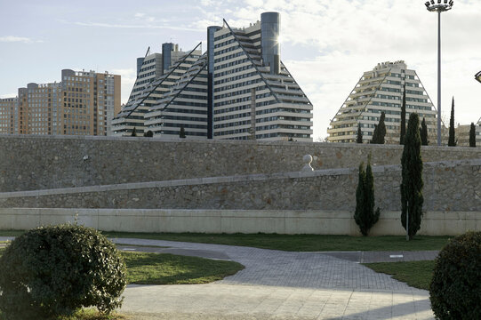 Modern triangular buildings with stone wall, trees, and path in urban landscape Valencia, Spain