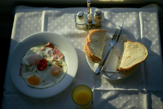 Breakfast table with fried eggs, sliced ham, tomatoes, bread, orange juice, and condiments, Prague, Czech Republic