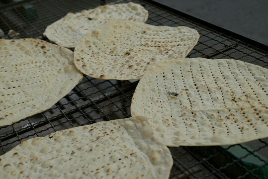 Thin flatbreads with perforated patterns baking on a metal rack outdoors. Tehran, Iran