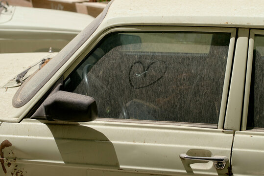 An old dusty car window with a heart drawn into the dirt on the glass surface. Tehran, Iran
