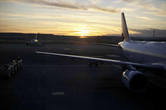 Airplanes parked on the runway at sunset, with a dramatic sky in the background.