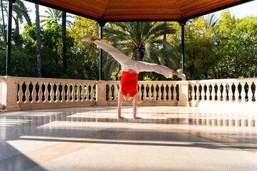 Young woman performing handstand with split legs in a gazebo