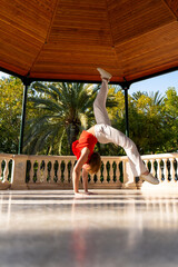 Young fitkid athlete performing handstand with leg split in gazebo