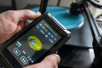 A pair of hands operates a 3D printer controller with a detailed display screen. Nijmegen, Netherlands