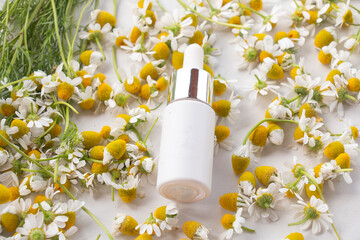 Bottle with essential oil, chamomile flowers, white surface, aromatherapy, spa treatments. Herbal medicine