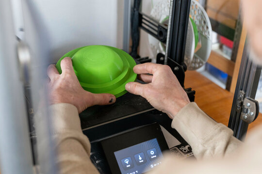 Person places a green plastic container on a 3D printer platform, adjusting its position. Nijmegen, Netherlands