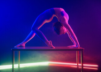 Woman performing a backbend on a table under vibrant blue and purple stage lights.