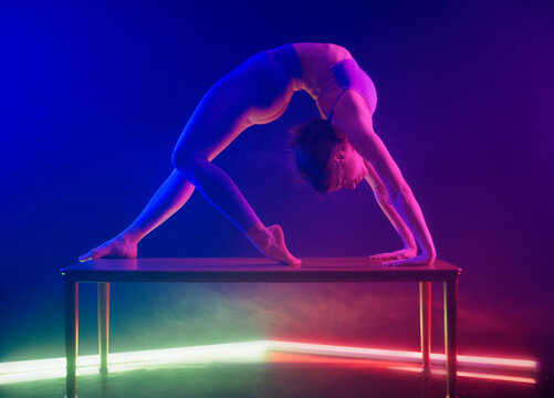 Woman performing a backbend on a table under vibrant blue and purple stage lights.