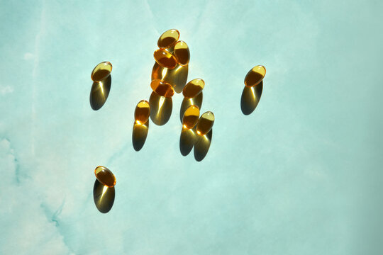 Many Golden Omega 3 Capsules under Sunlight on marble blue background