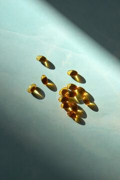 Many Golden Omega 3 Capsules under Sunlight on marble blue background