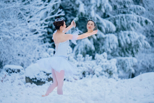 Ballerina in white tutu dancing on a snowy landscape, holding a circular mirror. WA, USA