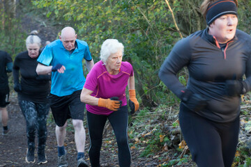 A group of people jogging uphill on a forest trail, dressed in athletic clothing appropriate for cool weather. Sale Water Park, Manchester, UK