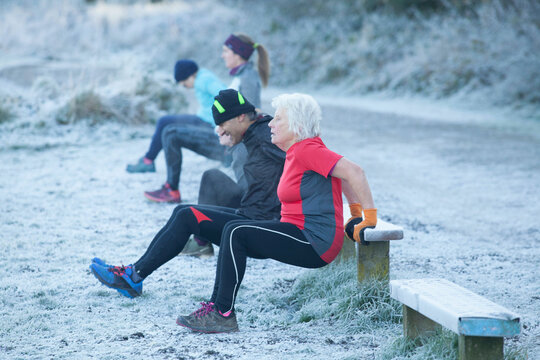 Four people exercise outdoors on a frosty morning, performing tricep dips on a bench beside a path. Sale Water Park, Manchester, UK