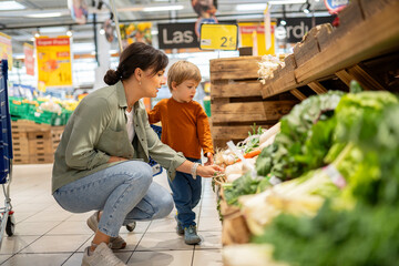 Mother and son choosing fresh vegetables in supermarket