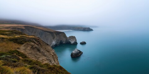 A foggy day with a rocky shoreline and a calm ocean. The sky is overcast and the water is a deep blue