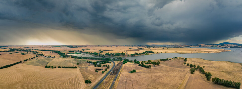 Large stormfront approaching over dry farmland and a reservoir
