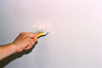 Man's hand painting the walls with a brush in a milky color.