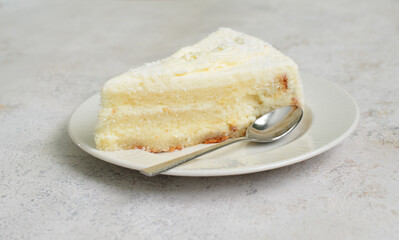 Delicious slice of white cake with coconut flakes on a plate with a spoon