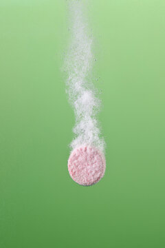 Effervescent Tablet Fizzing in Water on Green Background