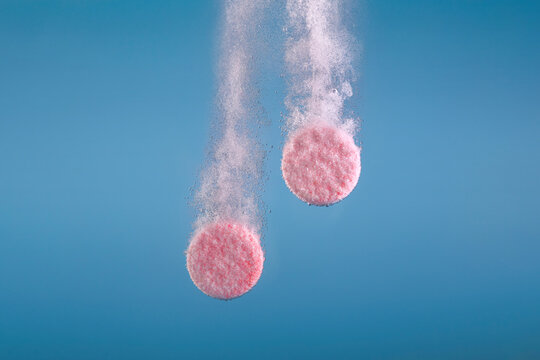 Effervescent Pink Tablets Dissolving in Water on Blue Background