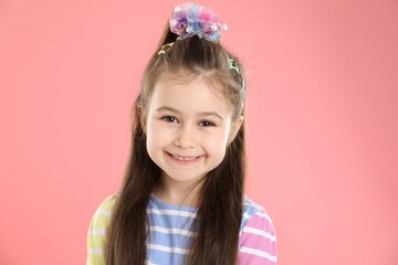 Happy little girl wearing beautiful hair accessories on pink background