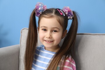 Happy little girl wearing beautiful hair accessories in armchair at home