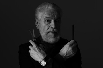 Bearded man with scissors and comb on dark background. Black and white effect