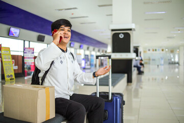 Happy Muslim Man Having Phone Call While Sitting and Waiting for Flight at Terminal Corridor. Mudik on Ramadan Moment Concept.