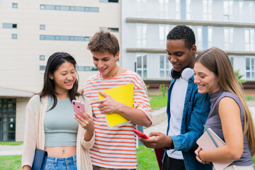 Group of cheerful students engaging with mobile devices while sharing exciting information and...