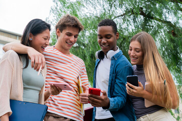 Group of enthusiastic young friends sharing exciting moments while looking at their smartphones together, enjoying laughter and camaraderie in a vibrant social setting outdoors