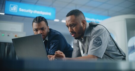 Airport Security Checkpoint: African American Security Officers Using Laptop Computer and Talking....